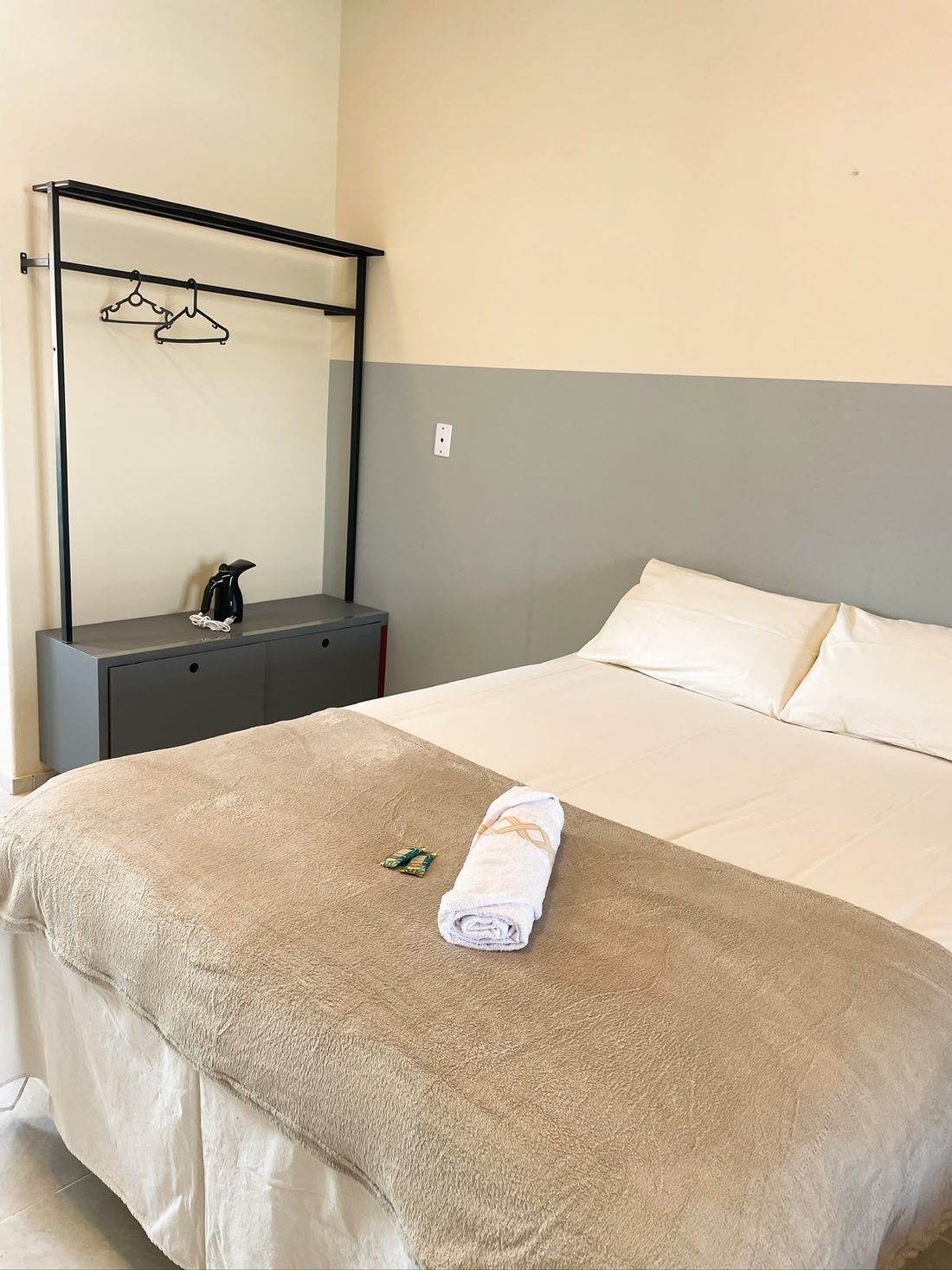 Quarto com cama de casal, roupeiro aramado e toalhas dobradas
